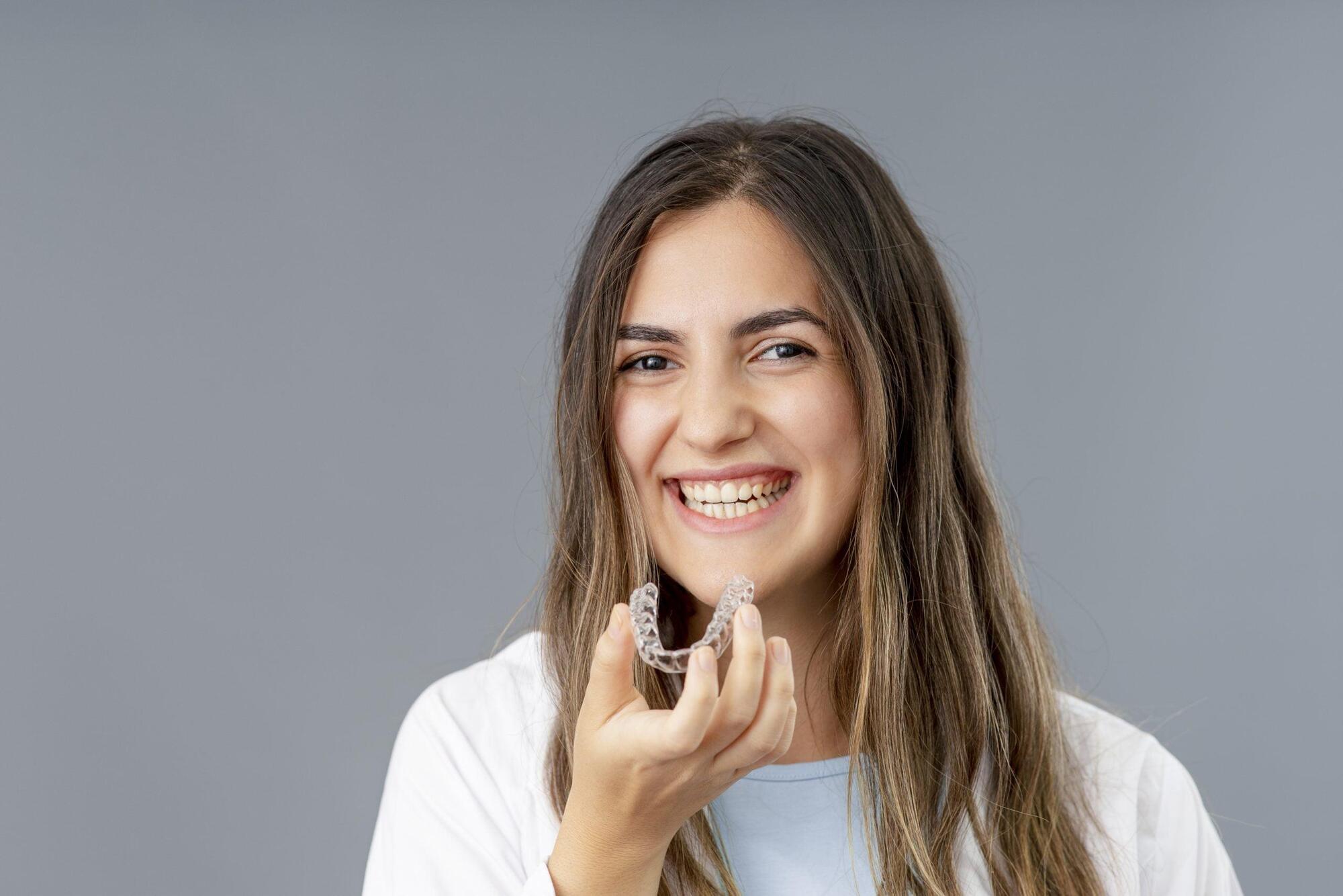 beautiful-smiling-turkish-woman-is-holding-invisalign-bracer-grey-background-studio-with-copy-space-scaled