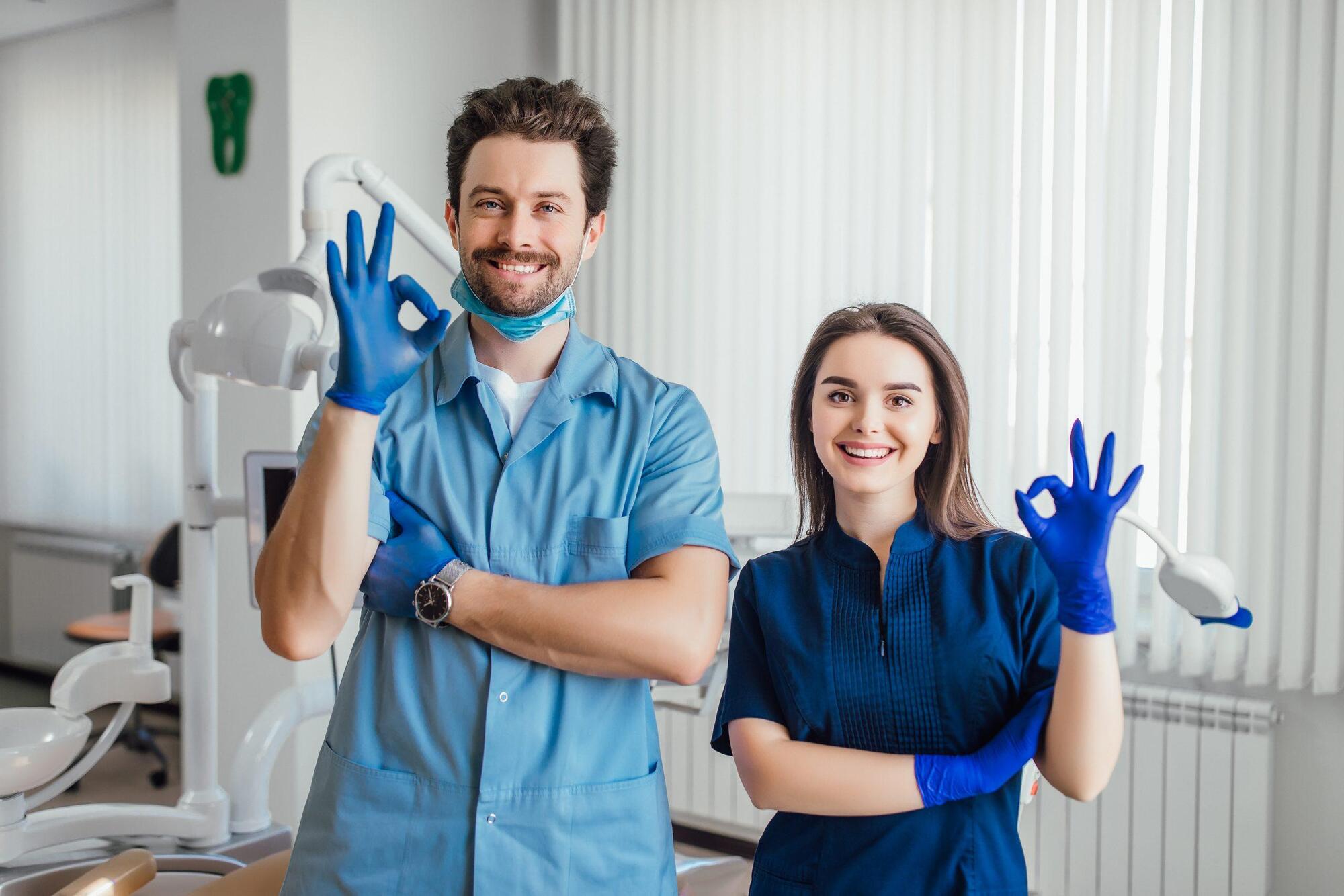 photo-smiling-dentist-standing-with-arms-crossed-with-her-colleague-showing-okay-sign-scaled